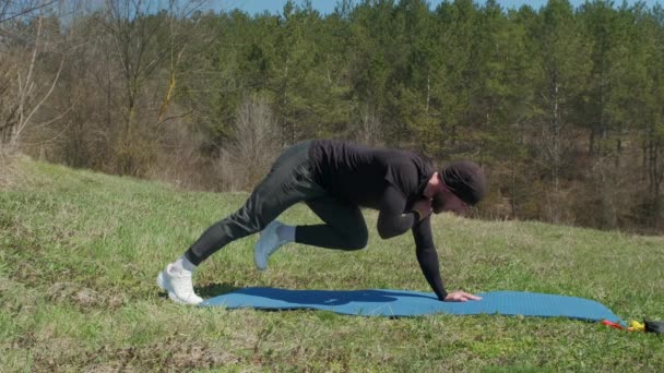 Playful sportsman extends leg behind him on fitness mat in the park — Stock Video