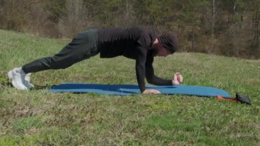 Oyuncu sporcu, parkta spor minderinde bacağını uzatıyor.