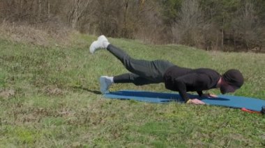 Oyuncu sporcu, parkta spor minderinde bacağını uzatıyor.