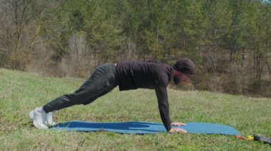 Oyuncu sporcu, parkta spor minderinde bacağını uzatıyor.