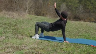 Oyuncu sporcu, parkta spor minderinde bacağını uzatıyor.