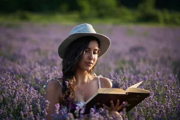 戴帽子的美女坐在紫色的薰衣草地里看书 — 图库照片