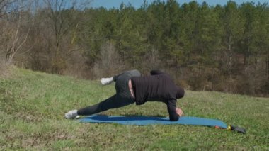 Oyuncu sporcu, parkta spor minderinde bacağını uzatıyor.