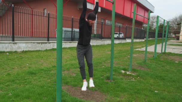 スポーツウェアを着た若者が街のスポーツ場の水平なバーで身を引く — ストック動画