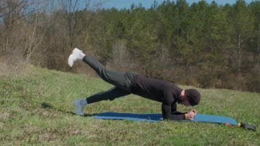 Oyuncu sporcu, parkta spor minderinde bacağını uzatıyor.