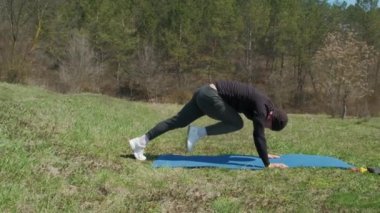 Oyuncu sporcu, parkta spor minderinde bacağını uzatıyor.