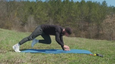 Oyuncu sporcu, parkta spor minderinde bacağını uzatıyor.