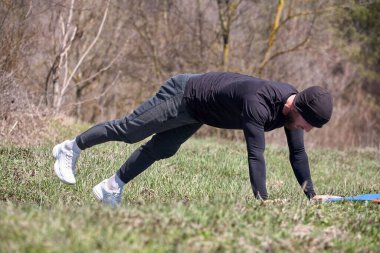 Oyuncu sporcu, parkta spor minderinde bacağını uzatıyor.