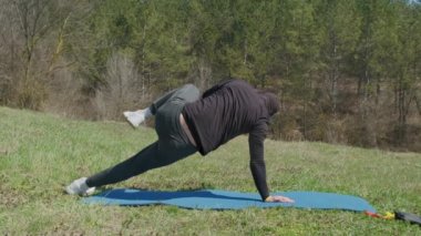 Oyuncu sporcu, parkta spor minderinde bacağını uzatıyor.