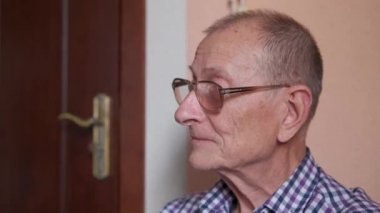Evin verandasında oturan yaşlı adam. Emekli adam yüzünü kameraya çevirir, gülümser, konuşur..
