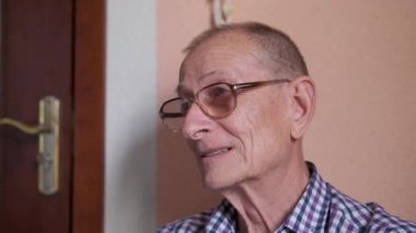 Evin verandasında oturan yaşlı adam. Emekli adam yüzünü kameraya çevirir, gülümser, konuşur..