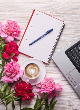 Kadın ofis masası dümdüz uzanıyordu. Dizüstü bilgisayarı olan bir kadın çalışma alanı, pembe şakayık buketi ve beyaz arka planda kahve. Üst görünüm kadınsı arkaplan.