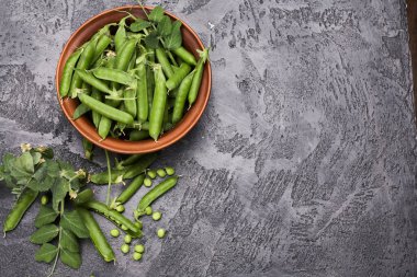 Yeşil bezelye kabukları ve gri tavan arasında yapraklar.