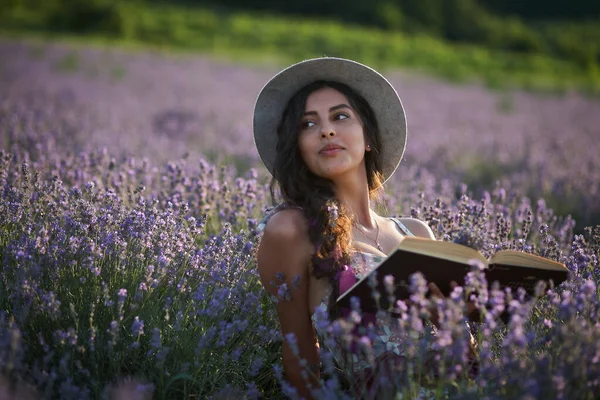 戴帽子的美女坐在紫色的薰衣草地里看书 — 图库照片