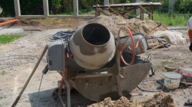 Küçük inşaat alanındaki kum yığınının yanında eski kirli beton karıştırıcı. Evde küçük taşınabilir çimento karıştırma makinesi. İnşaat alanı