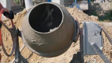 Küçük inşaat alanındaki kum yığınının yanında eski kirli beton karıştırıcı. Evde küçük taşınabilir çimento karıştırma makinesi. İnşaat alanı