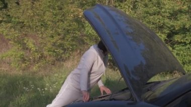 Bozuk bir arabanın yanında duran genç bir kadın sürücü kaputu patlamış ve yardım gelmesini bekliyor..