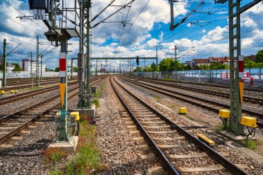 Rail tracks platform under dramatic clouds, expansive commuter hub with overhead catenary, sunlit concrete,