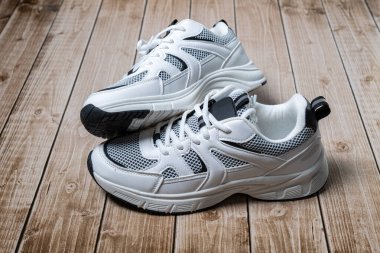 Ahşap zemindeki Whit ayakkabı çifti beyaz spor ayakkabıları ve zıt örgüler gösteriyor.