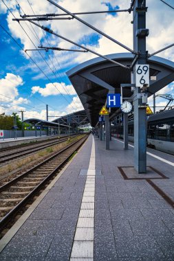 Rail tracks platform under dramatic clouds, expansive commuter hub with overhead catenary, sunlit concrete,