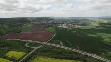 Parlak Tecavüz Tohumu, Canlı Sarı Kanola Blokları Taze Ted Toprak, Kesişen Karayolları ve Şehir Yolları, Ufuktaki Küçük Kasaba Çatıları 'na bitişik Hava Yamaları,