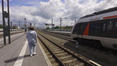 Tren istasyonunda bir kadın banliyö trenlerinin yanındaki platformda yürüyor. Kentsel yaşamda günlük toplu taşıma kullanımı.