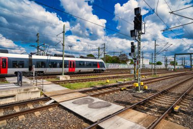 Rail tracks platform under dramatic clouds, expansive commuter hub with overhead catenary, sunlit concrete,
