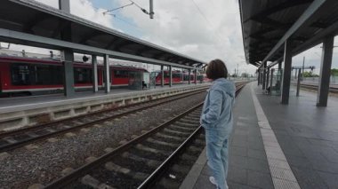 30.05.2025 Erfurt, Almanya. Tren istasyonunda bir kadın banliyö trenlerinin yanındaki platformda yürüyor. Kentsel yaşamda günlük toplu taşıma kullanımı.