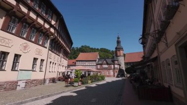 Schloss Stolberg, Almanya. 05.07.2025. Çakıl taşı meydanındaki tarihi ahşap evler, güneşli dekoratif cepheler ve dik gablı çatılar sessiz pazar manzarası, açık kafe oturma, klasik tabelalar.