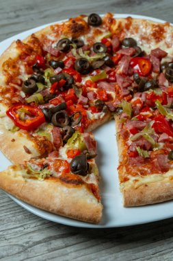 Bir dilimli pizza, davet edici, ayrık üçgen, yapışkan peynir çekimini gösteriyor, görünür zeytin, jambon ve biber sosları, gri masada sıcak altın kabuk, anı paylaşmayı ve aşermeyi öneriyor.