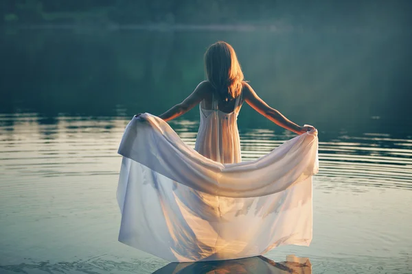 Mujer con vestido blanco en un lago al atardecer — Foto de Stock