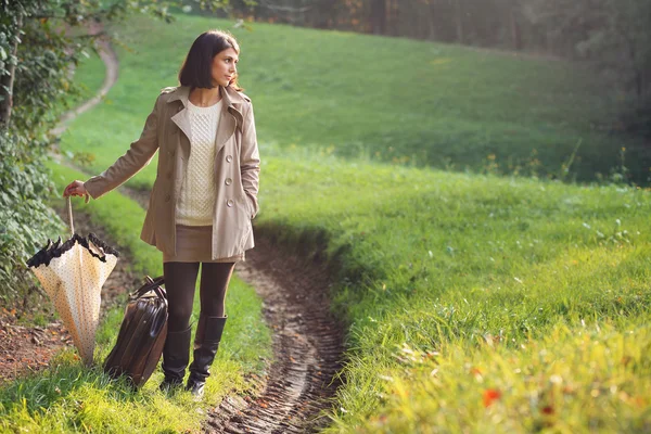 Mujer elegante en un camino de campo con maleta —  Fotos de Stock