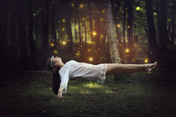 Woman levitation in the forest surrounded by fairies . Fantasy and surreal