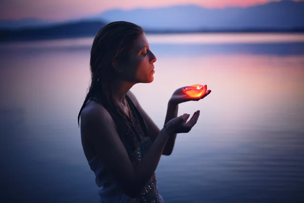 Beautiful woman lighted by candle in purple lake waters Royalty Free Stock Images