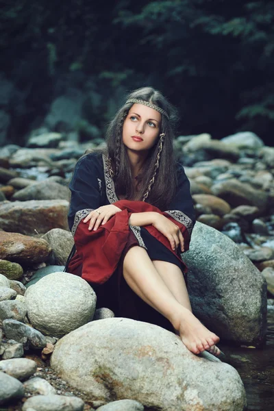 Красива середньовічна жінка сидить на каменях Стокове Фото