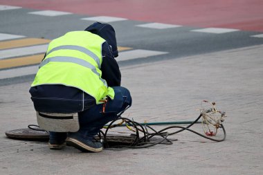 Sokakta açık kanalizasyon kapağında çalışan bir işçi. Elektrik ve iletişim onarımı, yeraltı hizmetleri, kablo döşeme