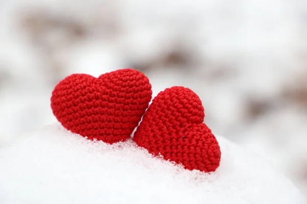 Love hearts, two red knitted symbols of passion in the snow drift. Background for Valentine\'s card