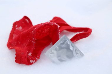 Karda kırmızı dantelli külot ve prezervatif. Kışın açık havada aşırı seks kavramı, doğum kontrolü.