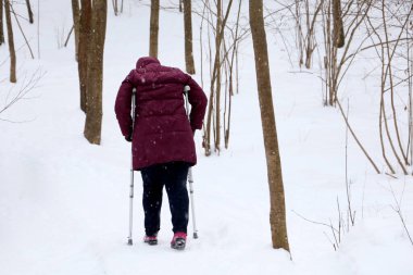 Kar yağarken elinde sopayla parkta yürüyen engelli bir kadın. Topal insan kavramı, sakatlık, sakatlık