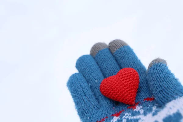 Red heart on palm of hand in warm knitted glove against the snow. Concept of a romantic love, Valentine\'s day or charity