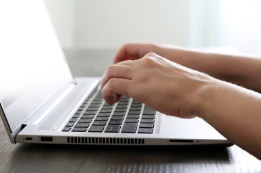 Dizüstü bilgisayarın üstündeki kadın elleri güneş ışığında masanın üstünde. Kadın, pencerenin yanında oturan dizüstü bilgisayarın klavyesinde uzaktan kumanda ile yazı yazıyor.