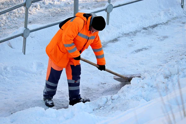 Kış şehrinde kar temizleme, sokak temizliği. Toplum hizmetleri görevlisi elinde kürekle kaldırımda kar temizliyor.