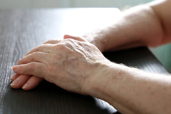 Wrinkled hands of elderly woman on a table close up. Concept of old age, arthritis, life at retirement