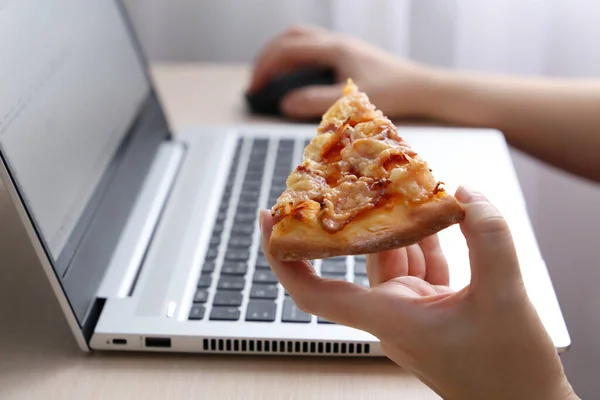 Dizüstü bilgisayarda pizza yiyen bir kadın, kadın eli kapalı. Büroda atıştırmalık, fast food.