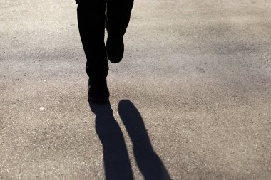 Sokakta koşan birinin silueti, kaldırımda koşan bir gölge. Spor ayakkabılı bir kadın kaldırımda koşar. Koşu konsepti, sağlıklı yaşam tarzı.