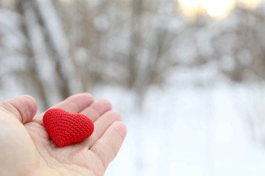 Kış ormanına karşı erkek avucunda kırmızı örülmüş bir kalp. Romantik aşk kavramı, Sevgililer Günü ya da hayırseverlik.