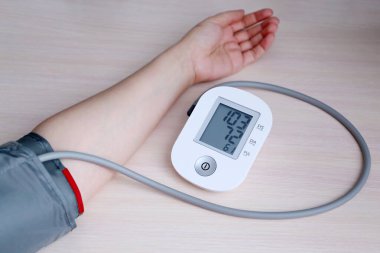 Kadın kan basıncını elektronik dijital tonometreyle ölçüyor, kadın eli yakın. Arteriyel hipotansiyon ve kardiyoloji konsepti