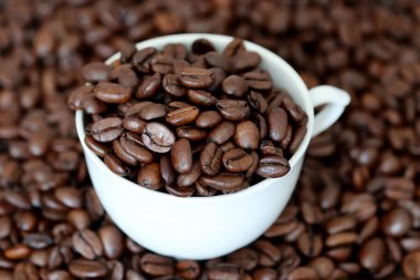 Beyaz fincanda kahve çekirdekleri. Koyu ve kavrulmuş, doğal içecek kavramı.