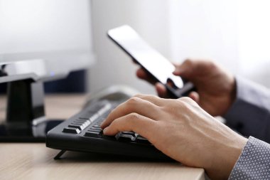 PC klavye geçmişinde akıllı telefon kullanan bir adam. Çevrimiçi iletişim, ofis veya ev işi ve ödeme kavramı