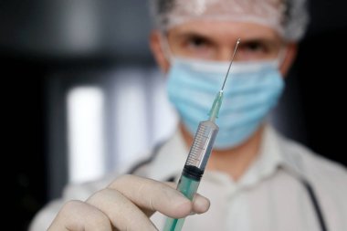 Doktor elinde şırınga, tıbbi maskeli adam ve enjeksiyona hazırlanan koruyucu eldivenler. Covid-19 salgını sırasında aşı kavramı